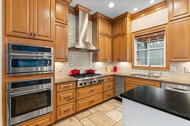 kitchen with tasteful backsplash, sink, light stone counters, stainless steel appliances, and wall chimney range hood