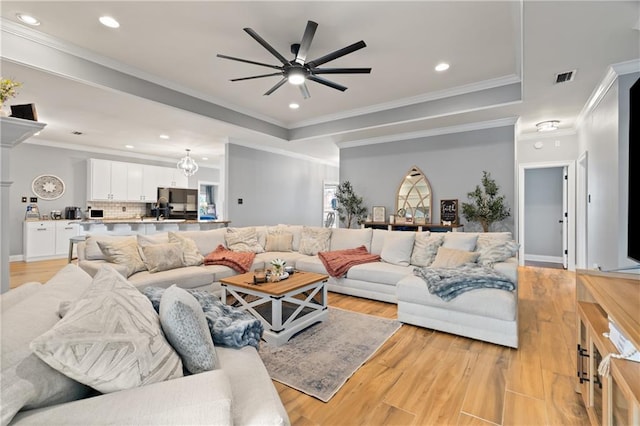 living room with crown molding, ceiling fan, light wood-type flooring, and a tray ceiling