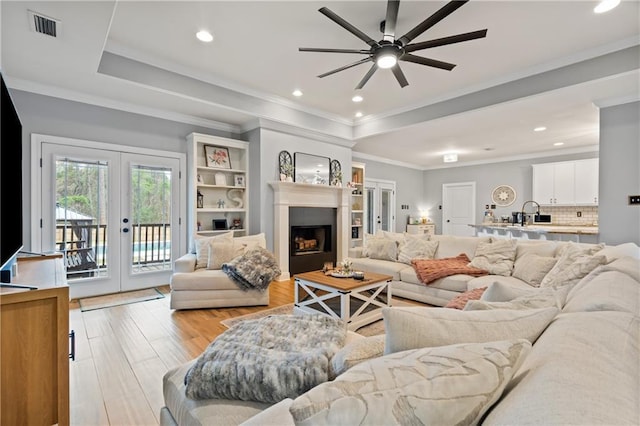 living room with a raised ceiling, crown molding, french doors, and light hardwood / wood-style flooring