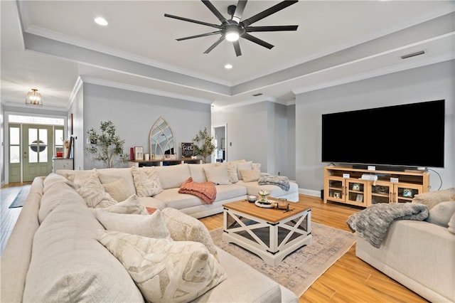 living room with hardwood / wood-style flooring, ceiling fan, ornamental molding, and a raised ceiling