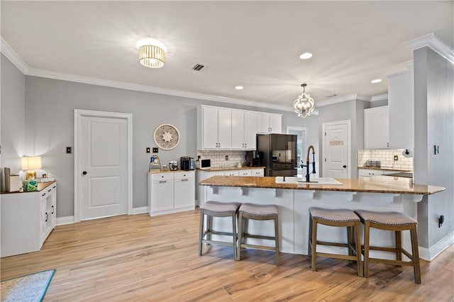 kitchen featuring a breakfast bar, sink, white cabinets, black fridge, and light stone countertops