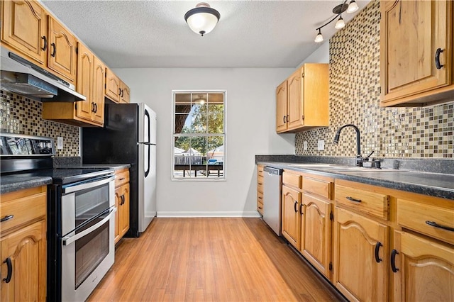 kitchen featuring decorative backsplash, appliances with stainless steel finishes, a textured ceiling, sink, and light hardwood / wood-style flooring