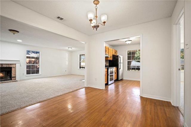 unfurnished living room featuring a fireplace, carpet floors, a chandelier, and a wealth of natural light