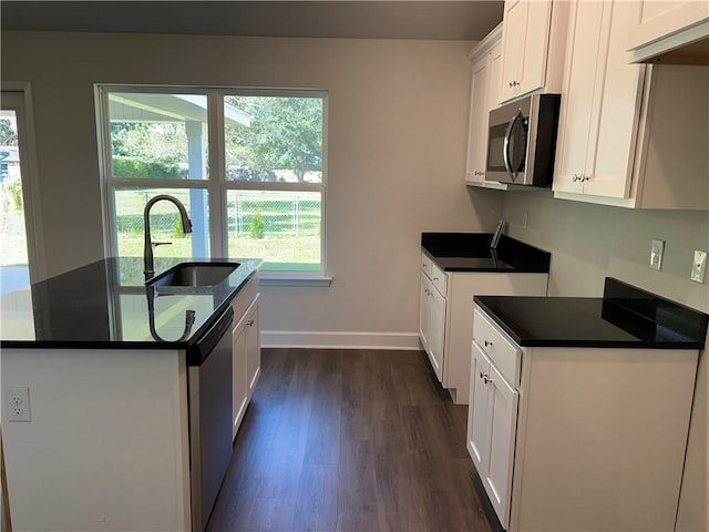 kitchen with appliances with stainless steel finishes, sink, white cabinets, dark hardwood / wood-style floors, and an island with sink