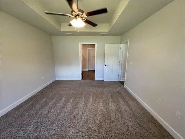 unfurnished bedroom with dark colored carpet, ceiling fan, and a raised ceiling