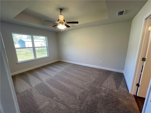 unfurnished room with a raised ceiling, ceiling fan, and dark carpet