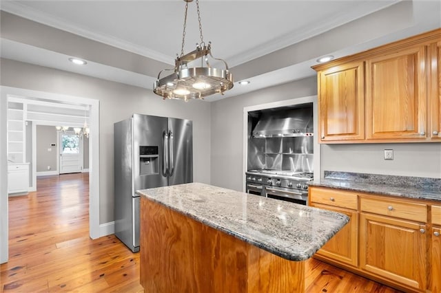 kitchen with stainless steel appliances, wall chimney range hood, light stone counters, light hardwood / wood-style flooring, and ornamental molding