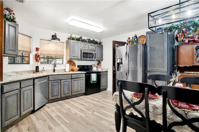 kitchen featuring light stone countertops, appliances with stainless steel finishes, sink, light hardwood / wood-style flooring, and gray cabinets