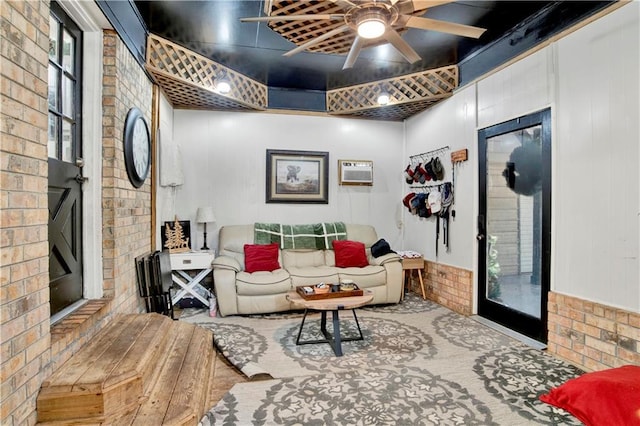 living room with a wall mounted air conditioner, ceiling fan, and brick wall