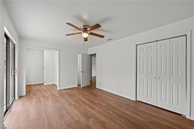 unfurnished bedroom featuring multiple closets, wood finished floors, visible vents, and baseboards