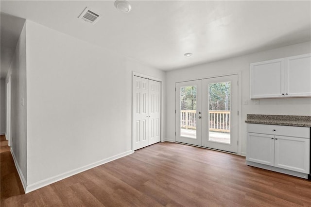 unfurnished dining area with wood finished floors, visible vents, french doors, and baseboards