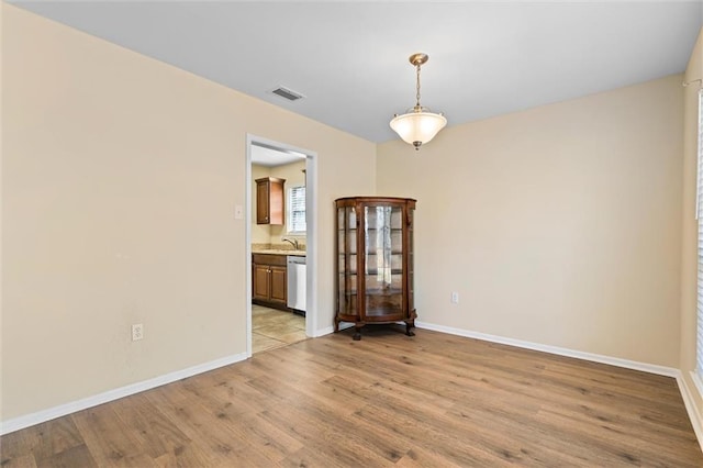 empty room with visible vents, a sink, light wood-style flooring, and baseboards