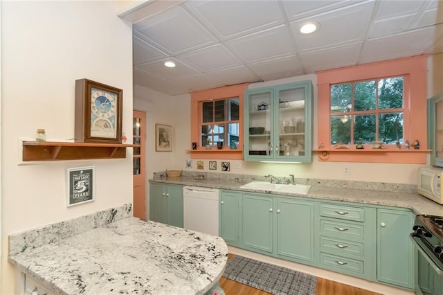 kitchen with green cabinetry, light hardwood / wood-style floors, light stone counters, sink, and white appliances