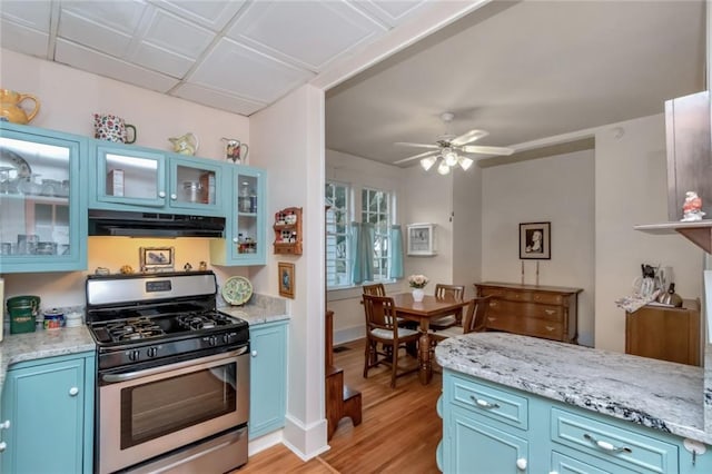 kitchen with light hardwood / wood-style floors, light stone counters, stainless steel range with gas cooktop, blue cabinetry, and ceiling fan