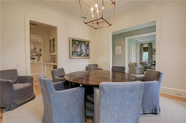 dining space featuring light hardwood / wood-style floors, ornamental molding, and an inviting chandelier