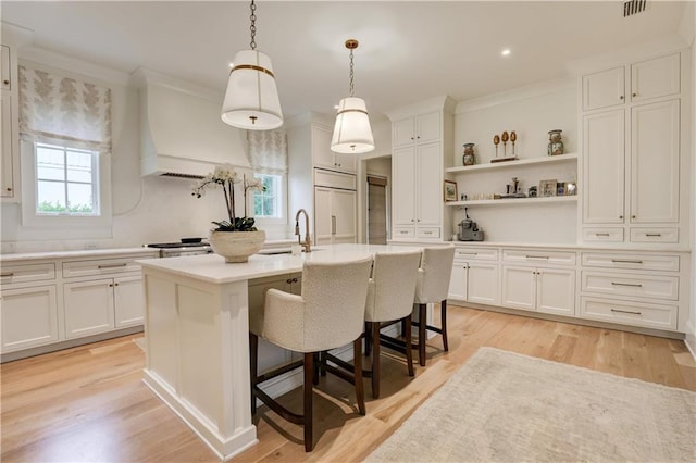 kitchen with a breakfast bar, pendant lighting, a center island with sink, light hardwood / wood-style floors, and white cabinetry