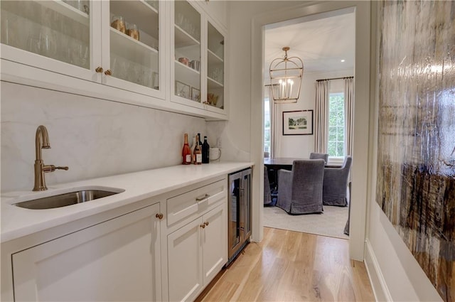 bar with white cabinetry, sink, light hardwood / wood-style flooring, crown molding, and decorative light fixtures