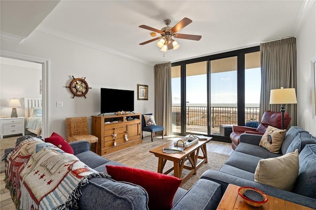 living room featuring light wood finished floors, a ceiling fan, a wall of windows, and crown molding