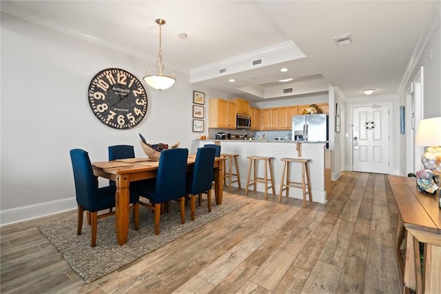 dining space featuring a tray ceiling, ornamental molding, and light hardwood / wood-style floors