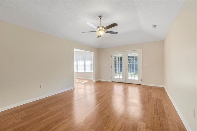 empty room featuring light wood-style flooring, a ceiling fan, visible vents, baseboards, and french doors