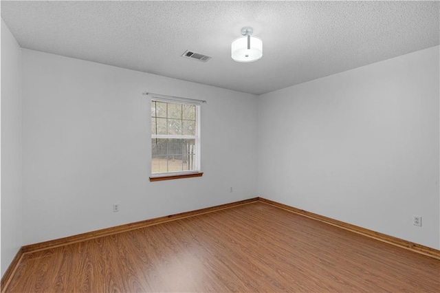 unfurnished room featuring visible vents, a textured ceiling, baseboards, and wood finished floors