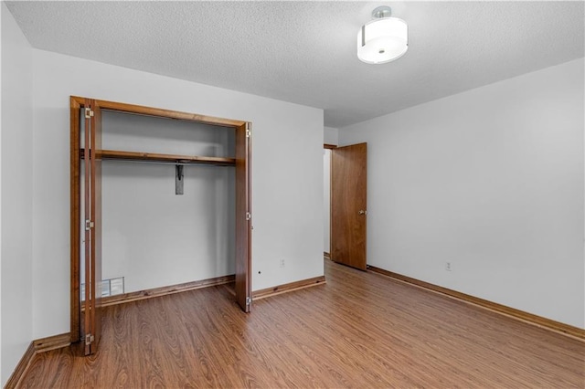 unfurnished bedroom featuring a closet, a textured ceiling, baseboards, and wood finished floors