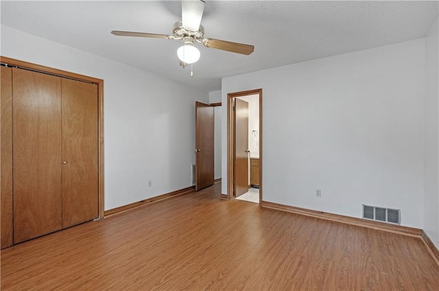 unfurnished bedroom with visible vents, ensuite bath, baseboards, and wood finished floors