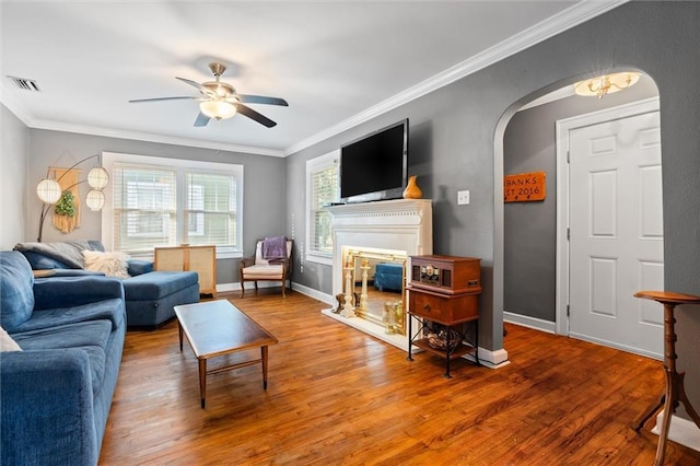 living room with arched walkways, visible vents, ornamental molding, and wood finished floors