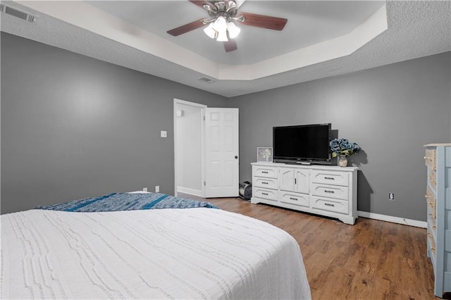 bedroom featuring a raised ceiling, baseboards, wood finished floors, and ceiling fan