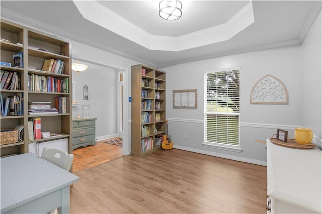 office area with light wood-style flooring, a tray ceiling, crown molding, and baseboards
