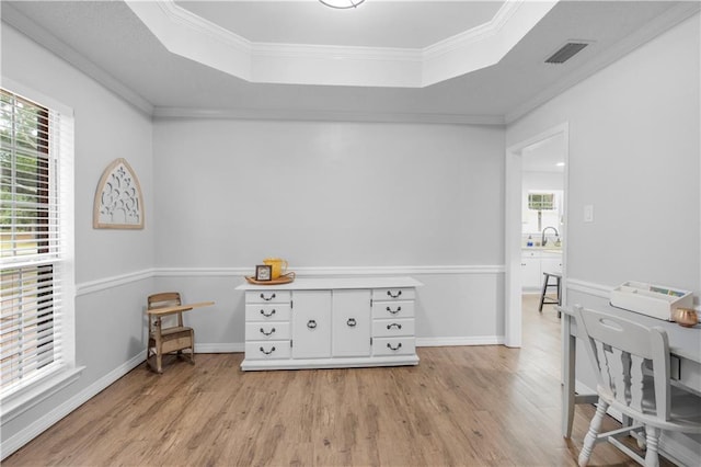 office area with light wood-style flooring, a tray ceiling, a sink, crown molding, and baseboards