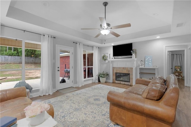 living area with a tray ceiling, a fireplace, a ceiling fan, wood finished floors, and recessed lighting