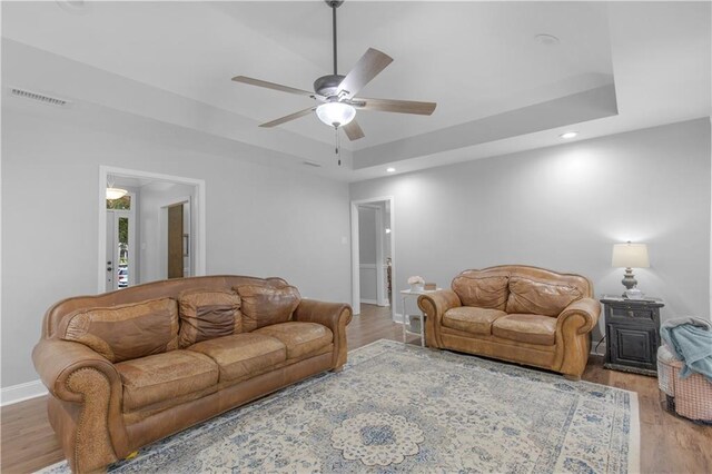 living room with ceiling fan, light wood finished floors, baseboards, recessed lighting, and a raised ceiling