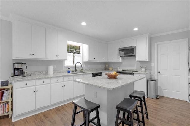 kitchen featuring stainless steel appliances, a sink, a kitchen bar, crown molding, and white cabinetry