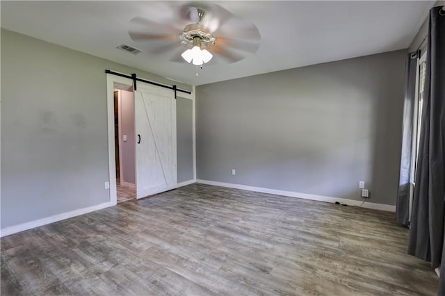 unfurnished bedroom featuring a barn door, ceiling fan, and hardwood / wood-style flooring