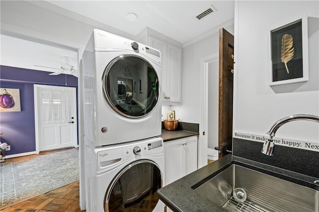 laundry area with cabinets, stacked washer / dryer, sink, ornamental molding, and ceiling fan