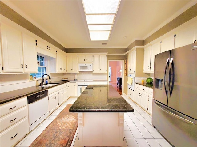 kitchen featuring white appliances, a kitchen island, dark stone counters, light tile patterned flooring, and a sink