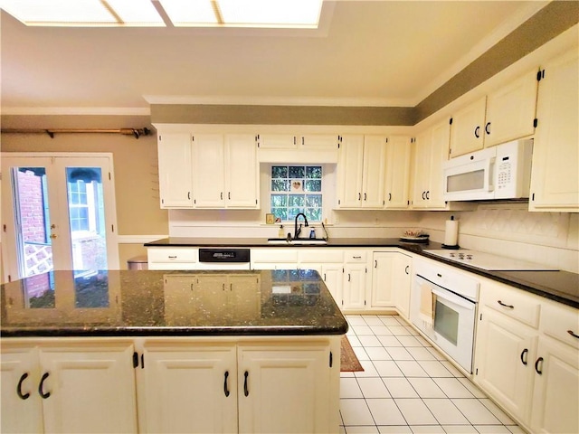 kitchen featuring white appliances, light tile patterned floors, dark stone counters, a sink, and white cabinetry