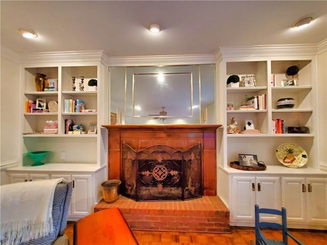 living area featuring crown molding, built in shelves, a fireplace with raised hearth, and wood finished floors