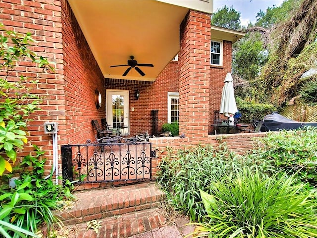 entrance to property with brick siding, a ceiling fan, and fence