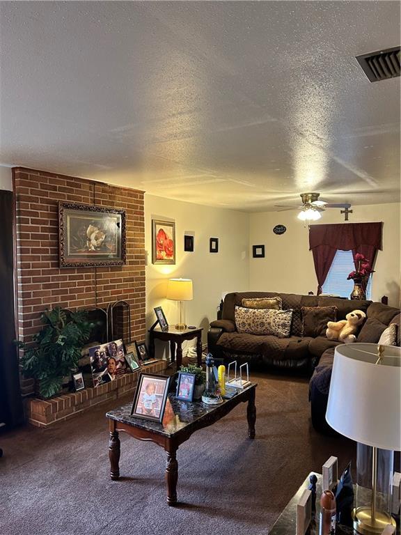 carpeted living room featuring ceiling fan, a fireplace, and a textured ceiling