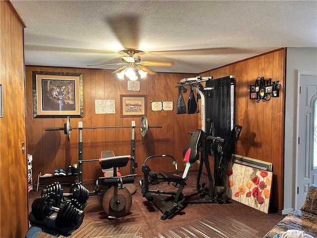 exercise room featuring carpet flooring, ceiling fan, wooden walls, and a textured ceiling