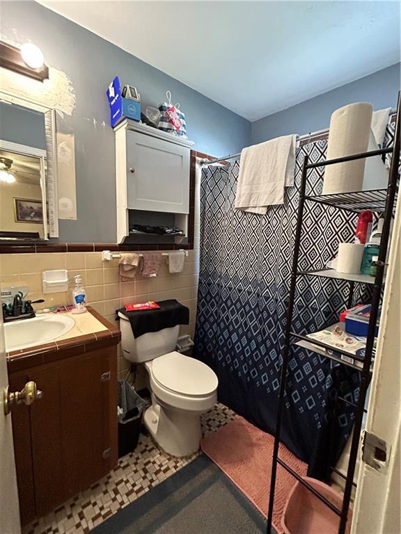 bathroom with a shower with shower curtain, vanity, toilet, and tile walls