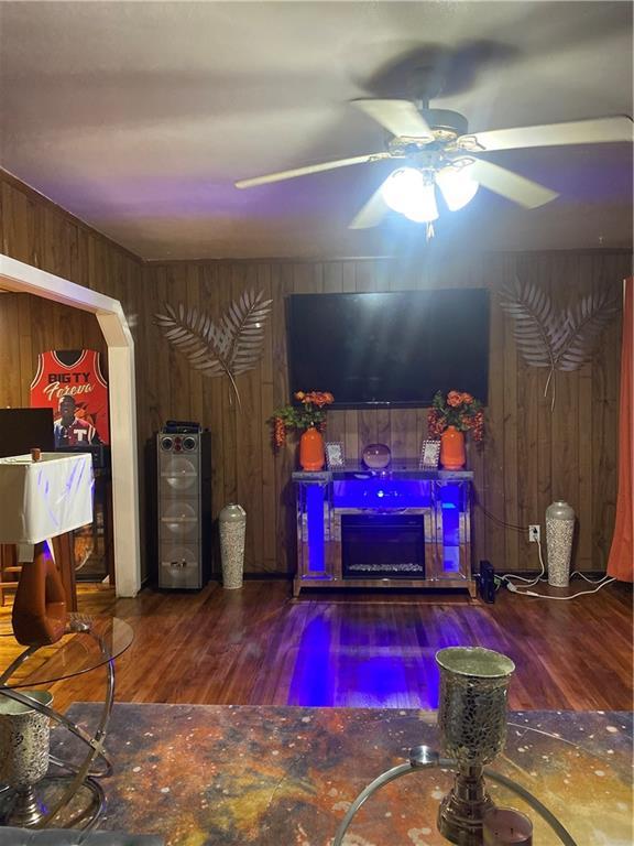 living room with wood walls, a fireplace, ceiling fan, and wood-type flooring