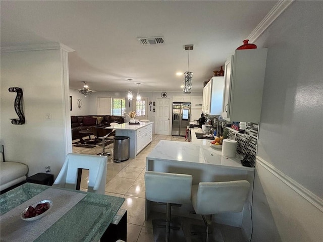 kitchen featuring stainless steel refrigerator with ice dispenser, ornamental molding, light tile patterned floors, decorative light fixtures, and white cabinets