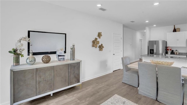 kitchen with stainless steel fridge, white cabinetry, light wood-style floors, recessed lighting, and a sink