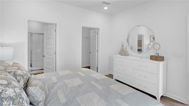 bedroom featuring a walk in closet, wood finished floors, baseboards, and ensuite bath