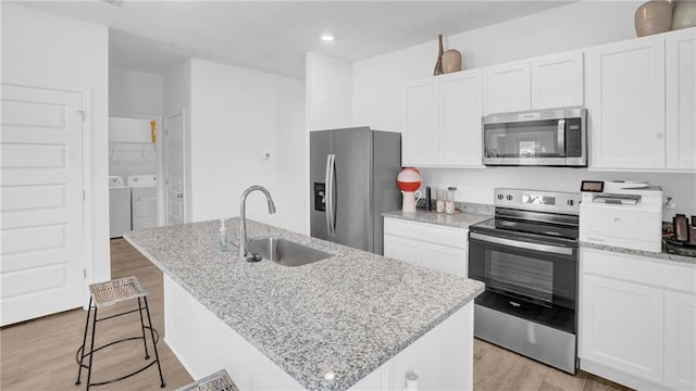 kitchen featuring stainless steel appliances, a sink, washer and clothes dryer, a center island with sink, and light wood finished floors