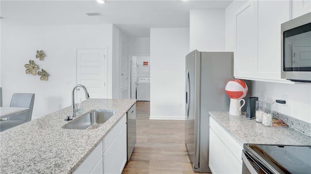 kitchen with washer / dryer, a sink, stainless steel appliances, light wood-style flooring, and white cabinetry