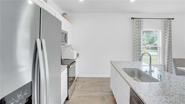 kitchen featuring appliances with stainless steel finishes, a sink, white cabinetry, light wood finished floors, and light stone countertops